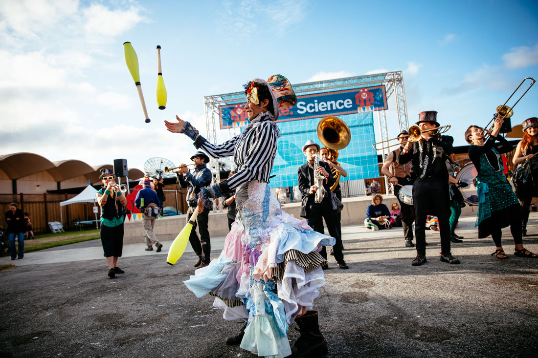 Performer juggling in front of a band of horn players at Maker Faire in San Mateo by Becca Henry Photography