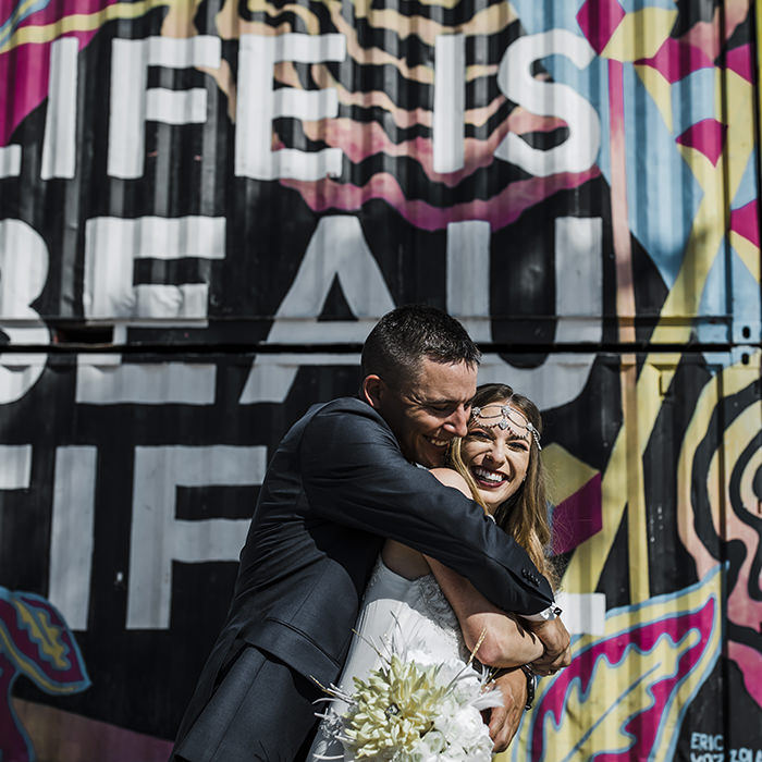 Las Vegas wedding – A newlywed couple shares a joyful embrace in front of a vibrant mural that reads 'Life is Beautiful,' capturing the energy and artistic spirit of their celebration.