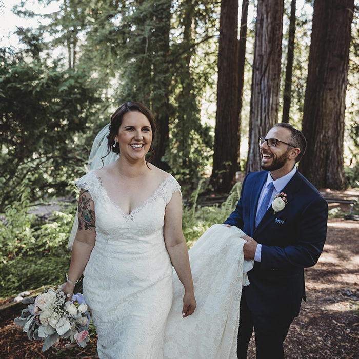 Bride and groom walk hand in hand through a serene wooded path at the Brazilian Room in Oakland, surrounded by towering trees and dappled sunlight.