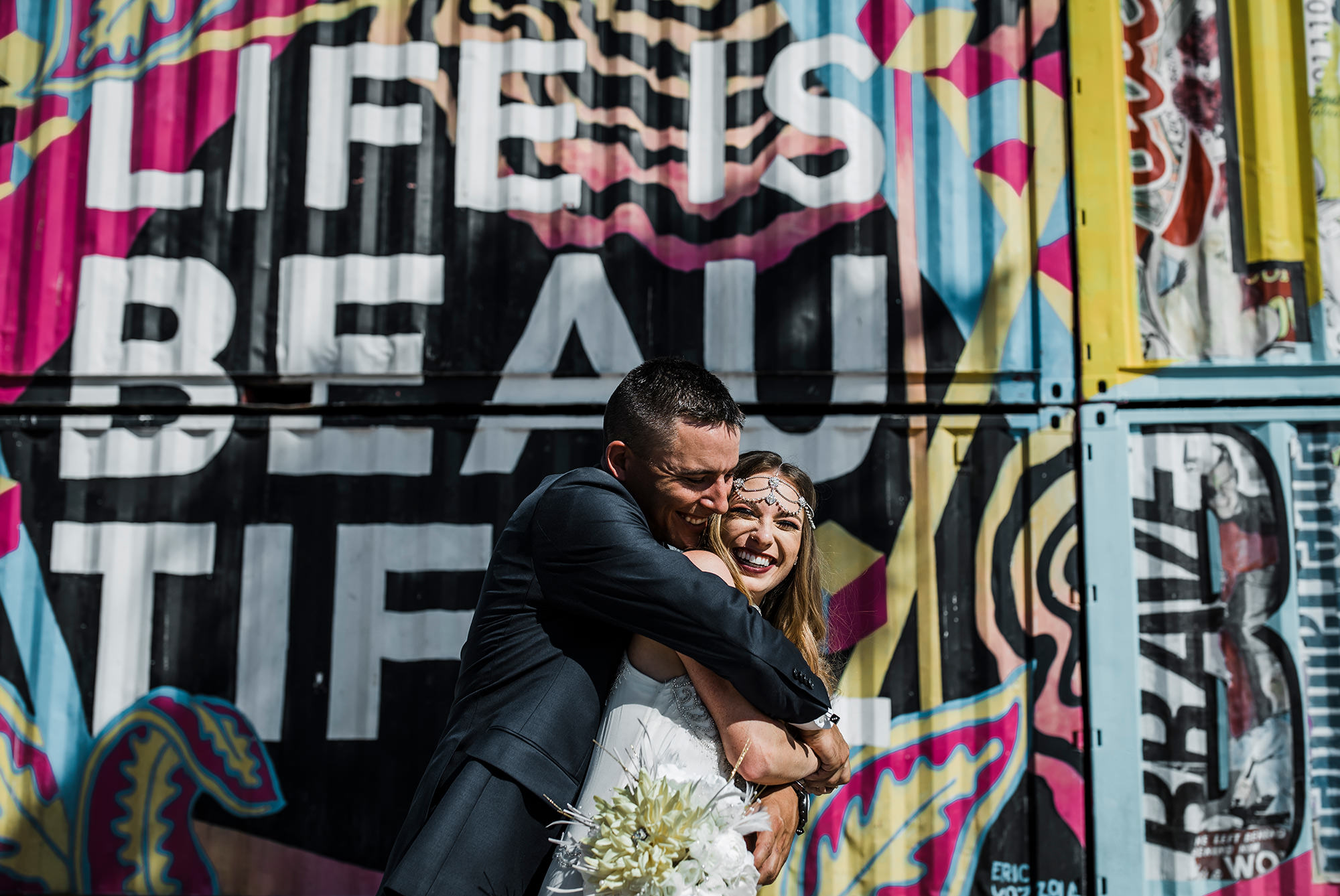 Bride and groom hugging in front of life is beautiful mural for Las Vegas Wedding -Becca Henry Photography-
