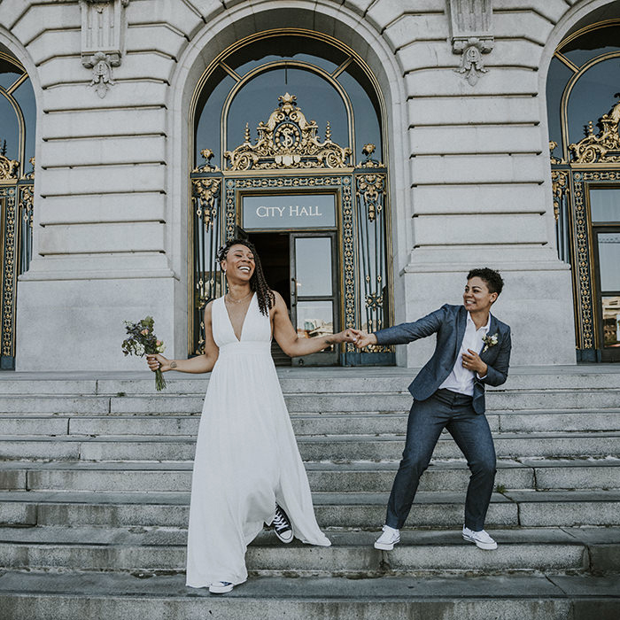 San Francisco City Hall Wedding – Two brides hold hands dancing on the grand steps in front of its elegant gold-accented doors
