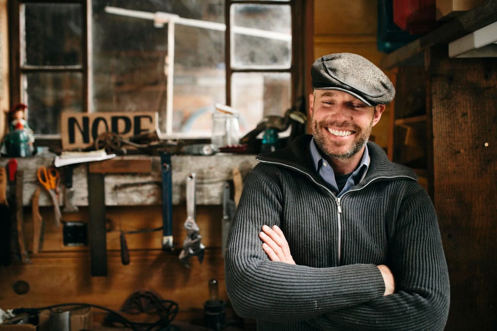 Smiling man in workshop with tools and wooden background, showcasing professional branding photograp.