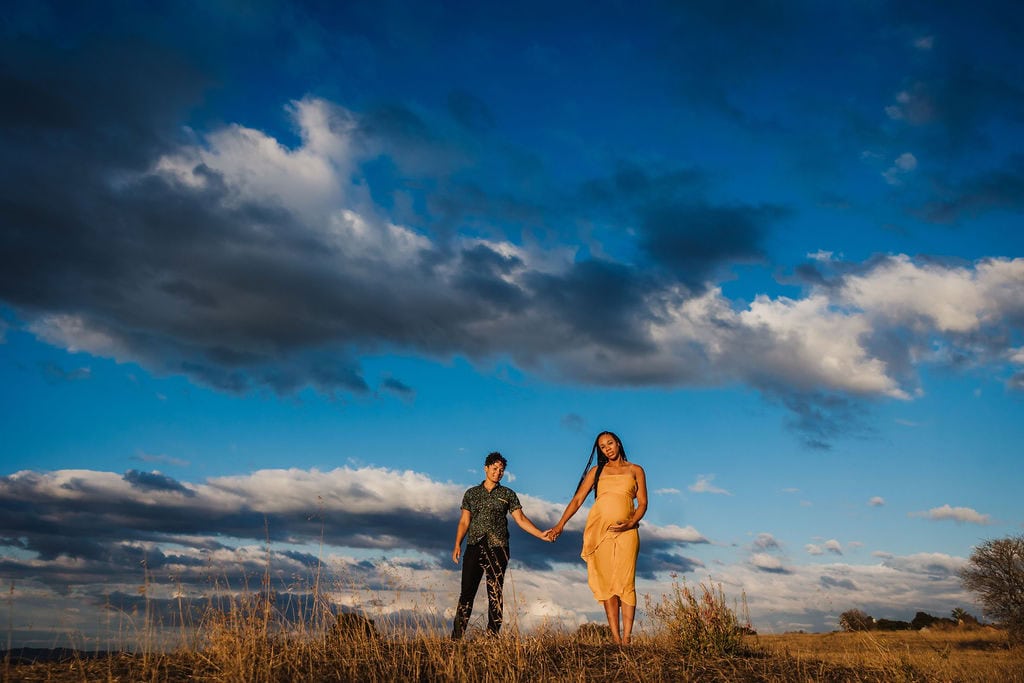 Couple holding hands outdoors with dramatic sky in the background.