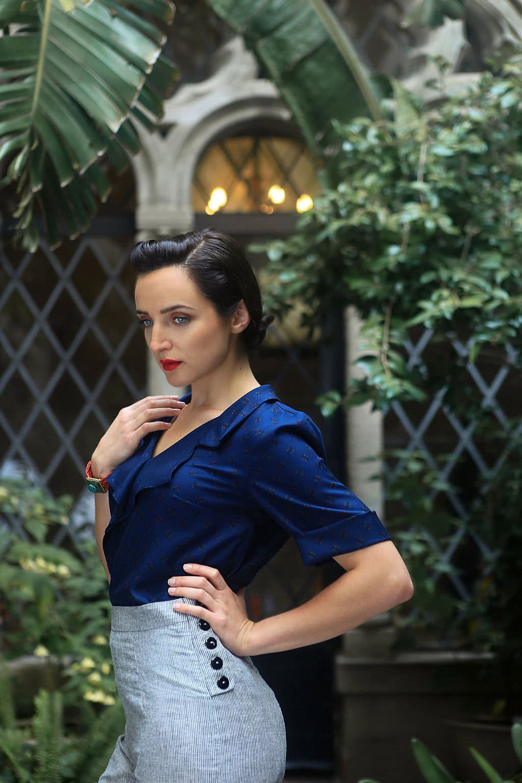 Elegant woman in blue blouse and gray skirt in lush garden setting.