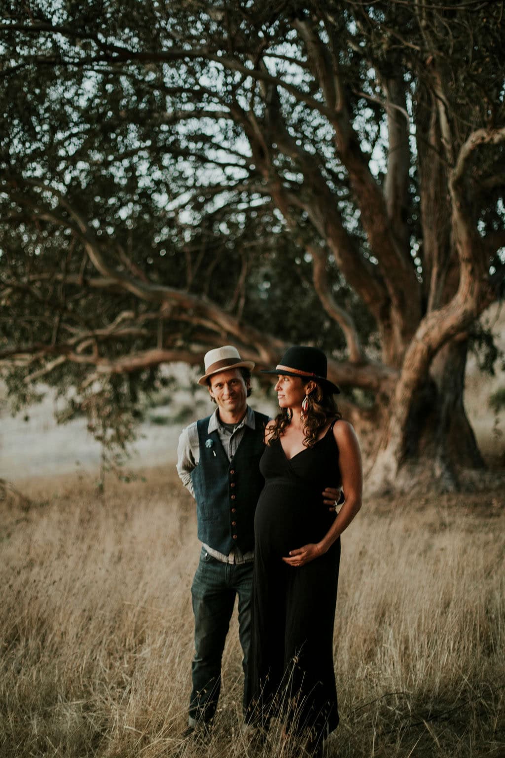 Pregnant woman and partner in a natural outdoor setting with large trees.