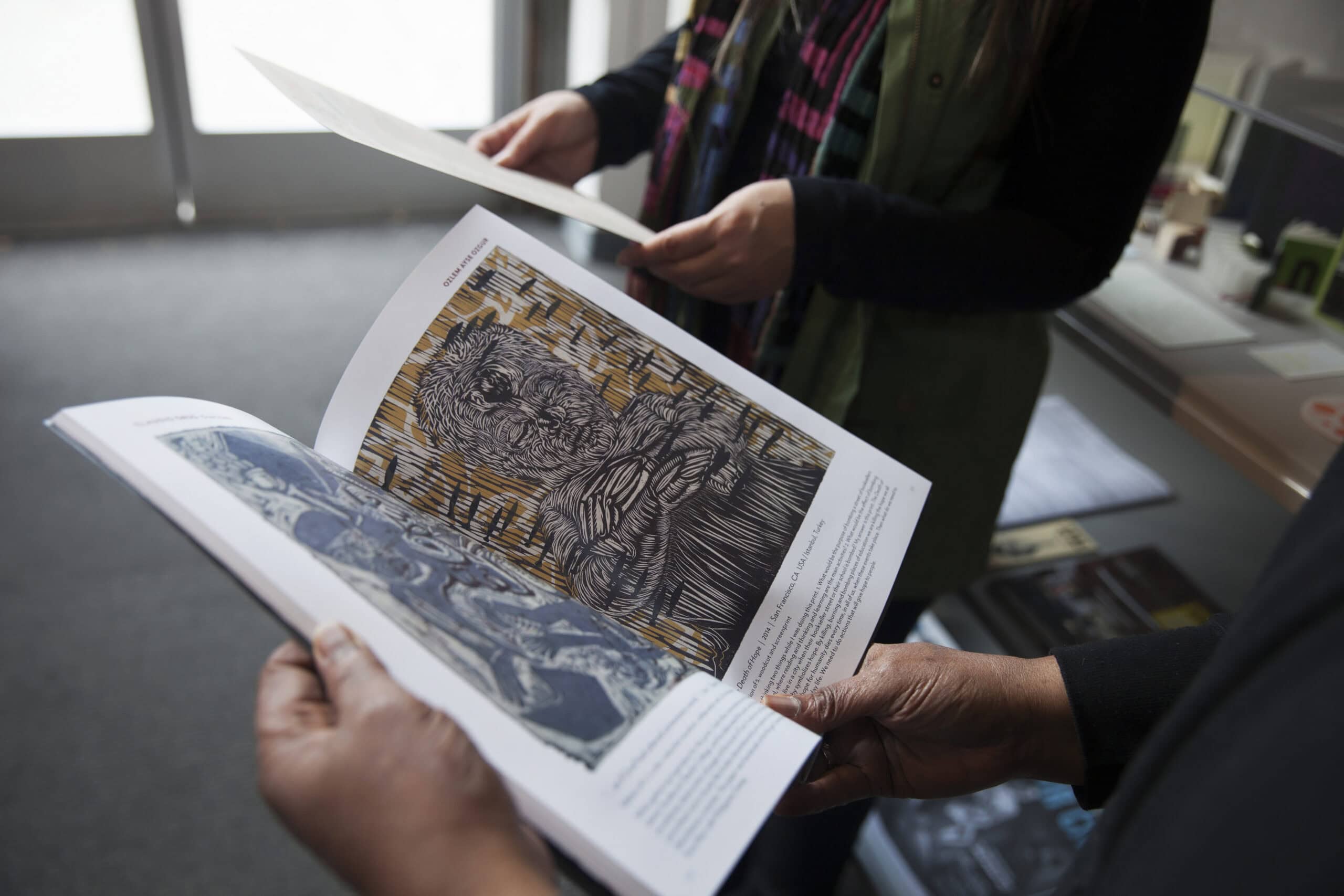 People reviewing a printed art catalog in an office setting.