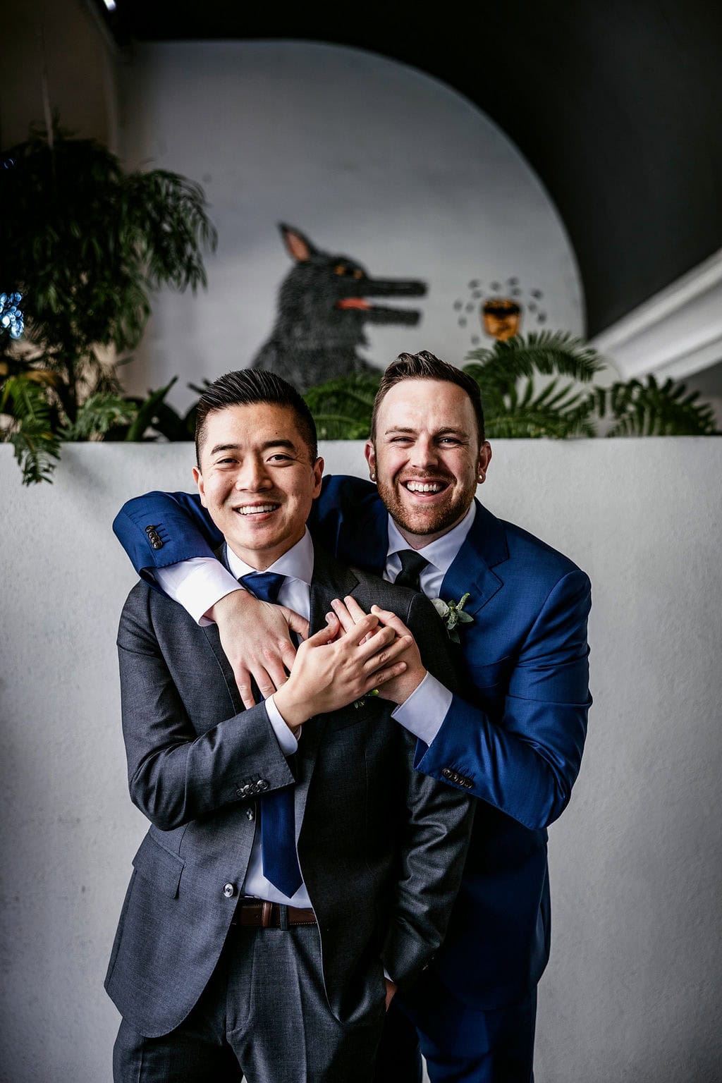 Two men in suits celebrating at a wedding with a dog in the background.